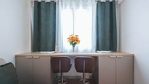 Une petite cuisine équipée avec une fenêtre, deux chaises et un vase avec des fleurs.