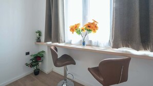 Una stanza con una finestra, un vaso con fiori, una pianta in vaso e due sedie.