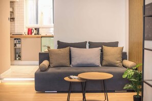 A modern living room with a sofa, a small round table, and a potted plant. - Spacious Studio King Bed & Workspace|Weekend Noise (Athens)