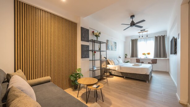 Una moderna camera d'albergo con un letto, un'area relax con divano e poltrone, un tavolino, una pianta e una ventola a soffitto.