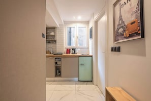 A compact kitchen with a built-in dishwasher, a window, and a poster of the Eiffel Tower. - Spacious Studio King Bed & Workspace|Weekend Noise (Athens)