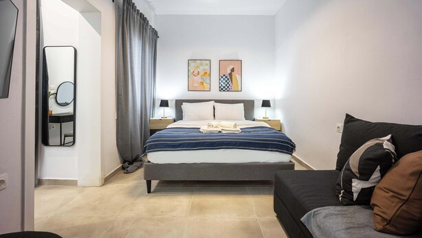 A modern bedroom with a bed, bedside tables, a mirror, and artwork on the wall. - Modern Studio | King Bed & Work Corner (Athens)