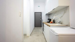 A narrow kitchen with white cabinets, a marble backsplash, and a coffee machine. - Modern Studio | King Bed & Work Corner (Athens)