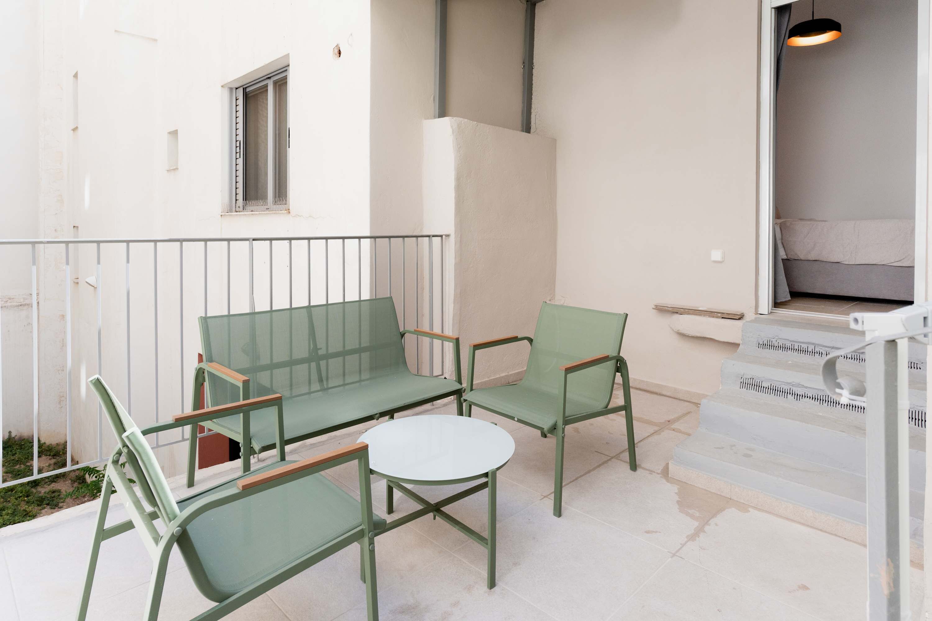 A patio with a green sofa, two chairs, and a small round table.