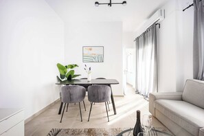 Un soggiorno moderno con un divano grigio, un'area pranzo con tavolo e sedie, e un'ampia finestra con tende.