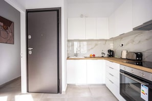 Une cuisine moderne avec des meubles blancs, un pare-feu en marbre, un réfrigérateur en acier inoxydable et un four encastré.