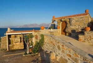 Ein Steinhaus mit Ziegeldach, einer Holztür und Blick auf das Meer.