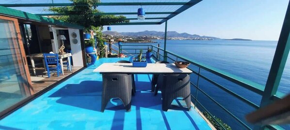 Ein Balkon mit Tisch und Stühlen, mit Blick auf ein Gewässer und das entfernte Land.