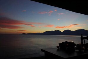 Ein Sonnenuntergangsblick von einem Balkon mit Blick auf ruhiges Wasser und entfernte Berge.
