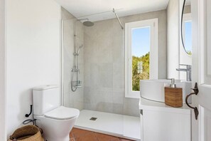 Ein modernes Badezimmer mit Dusche, Toilette und Waschbecken, mit einem Fenster und Blick auf Grünflächen.