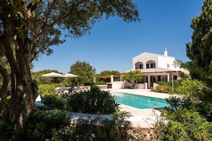 Eine weiße Villa mit Swimmingpool, umgeben von üppiger Vegetation und Bäumen.