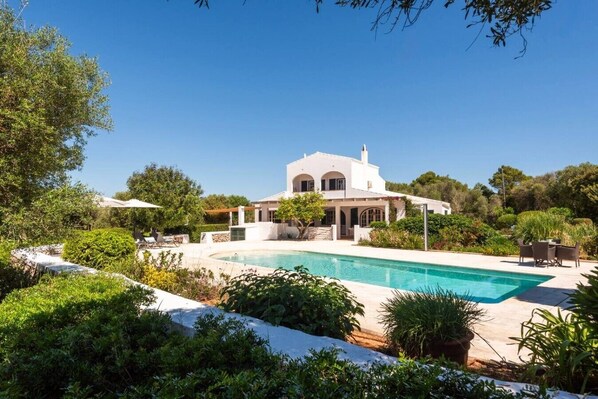 Eine weiße Villa mit Pool, umgeben von Grün und Bäumen.