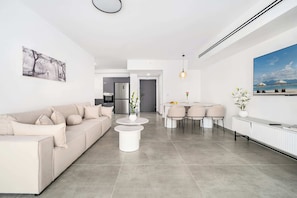 Ein modernes Wohnzimmer mit Sofa, Couchtisch, Essbereich, Küche und Kunstwerken an den Wänden.