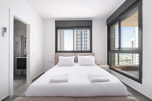 Ein modernes Hotelzimmer mit einem großen Bett, zwei Fenstern, Blick auf Gebäude und einem Badezimmer mit Dusche.