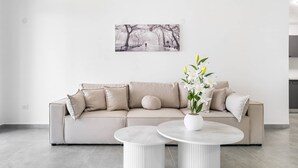 Een moderne zithoek met een beige bank, twee ronde tafels, een potplant en een aan de muur hangend schilderij.