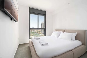 Ein modernes Hotelzimmer mit einem großen Bett, einem Fenster mit Blick auf die Stadt und einem wandmontierten Fernseher.