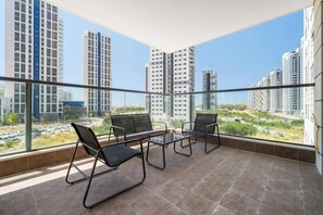 Ein Balkon mit Blick auf hohe Gebäude, einem Glastisch und schwarzen Stühlen.
