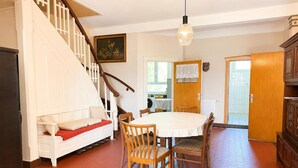 A dining area with a round table and chairs, a staircase, a wooden cabinet, and a painting on the wall. - Jagels-Hammann farm, fitters' apartment, An der Schule 6, 27607 Geestland (Geestland)