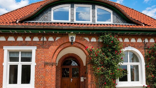 A brick building with a pitched roof, arched entrance, and a flower box with red flowers. - Jagels-Hammann farm, fitters' apartment, An der Schule 6, 27607 Geestland (Geestland)