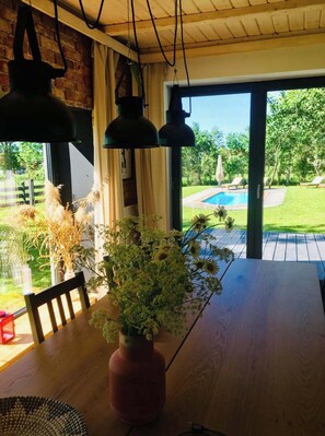 A wooden table with a vase of flowers, a chair, and hanging pendant lights.