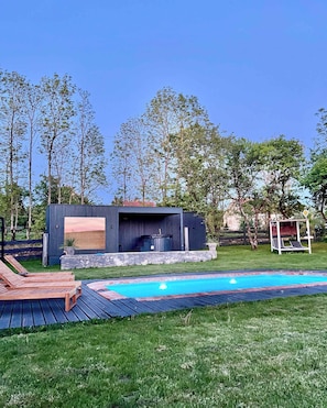 Ein Garten mit Swimmingpool, einer Holzterrasse und einer modernen Sitzgruppe im Freien.