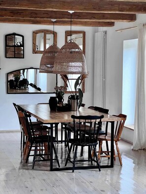 Un comedor con una mesa de madera, sillas negras y lámparas colgantes tejidas.