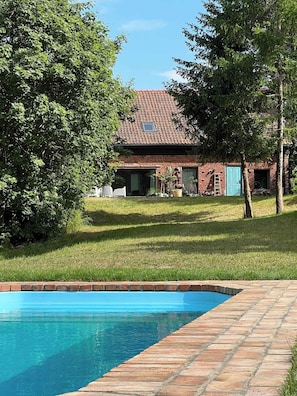 A house with a swimming pool, surrounded by trees and a grassy lawn.
