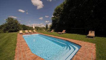 A rectangular swimming pool with a brick border, surrounded by a grassy lawn and trees.
