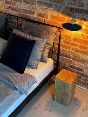Una cama con almohadas, una mesita de noche de madera y una pared de ladrillo.