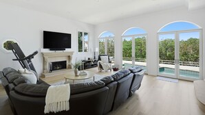 A modern living room with a fireplace, a large TV, and a view of a swimming pool. - 4BR Luxury Home with Private Pool & Jacuzzi (Los Angeles)