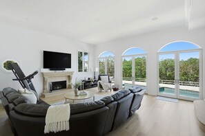 Ein modernes Wohnzimmer mit Kamin, großem Fernseher und Blick auf einen Swimmingpool.