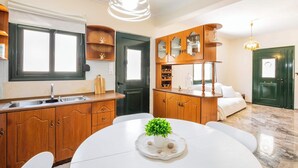Eine moderne Küche mit Holzschränken, einem weißen Esstisch und einem Blumentopf, sowie einer grünen Tür.