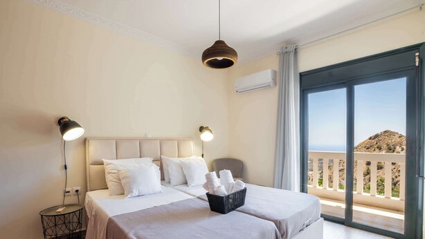 Ein Hotelzimmer mit einem Bett, Nachttischlampen, einem kleinen Tisch, einem Wäschekorb mit Handtüchern und einem Balkon mit Blick.