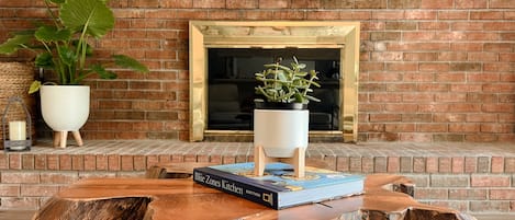 A wooden table with a book and a potted plant in front of a brick wall with a fireplace.