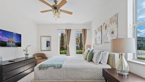 A bedroom with a bed, a ceiling fan, a TV, a dresser, a chair, and a window with curtains. - Lakefront 4BR Disney Home with Pool & Game Room (Kissimmee)