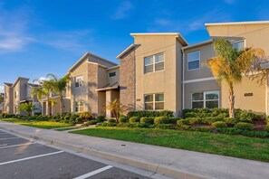 A row of modern multi-story buildings with a uniform architectural style, featuring balconies, windows, and a well-maintained lawn with small trees. - ChampionsGate Home Near Disney with Pool (Davenport)