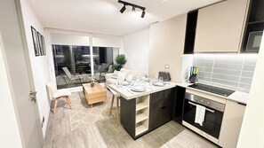 Eine moderne Küche mit Einbauherd, ein Essbereich mit Tisch für zwei Personen und ein großes Fenster mit Blick auf die Straße.