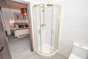 A modern bathroom with a glass-enclosed shower, a toilet, and a bed with a headboard in the background. - Spacious 1 Bedroom Apartment in Central Wakefield (Wakefield)
