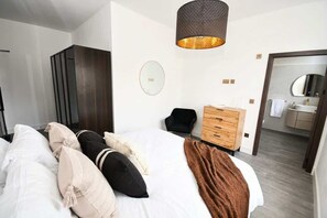 A hotel room with a large bed, a wooden dresser, a mirror, and a hanging light fixture. - Cozy Central Wakefield 1BR Apt (Wakefield)
