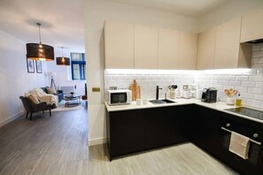 Eine moderne Küche mit schwarzem Arbeitsplatz, weißem Fliesenspiegel und einem Essbereich mit Sofa und Couchtisch.