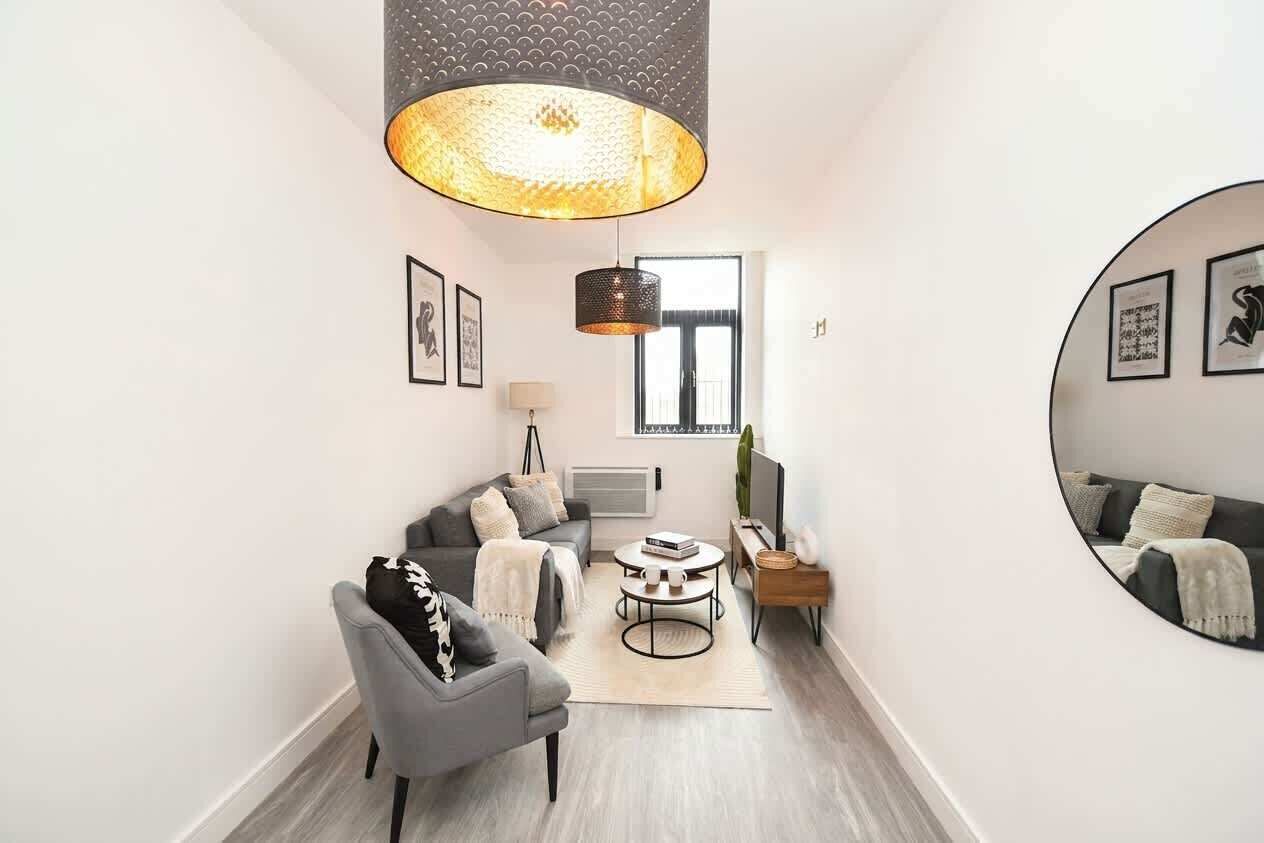 Un salon moderne avec un canapé gris, une table basse ronde et un grand miroir au mur.