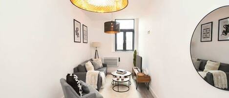 Un salon moderne avec un canapé gris, une table basse ronde et un grand miroir au mur.