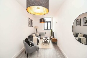 A modern living room with a grey sofa, a round coffee table, and a large mirror on the wall. - Cozy Central Wakefield 1BR Apt (Wakefield)
