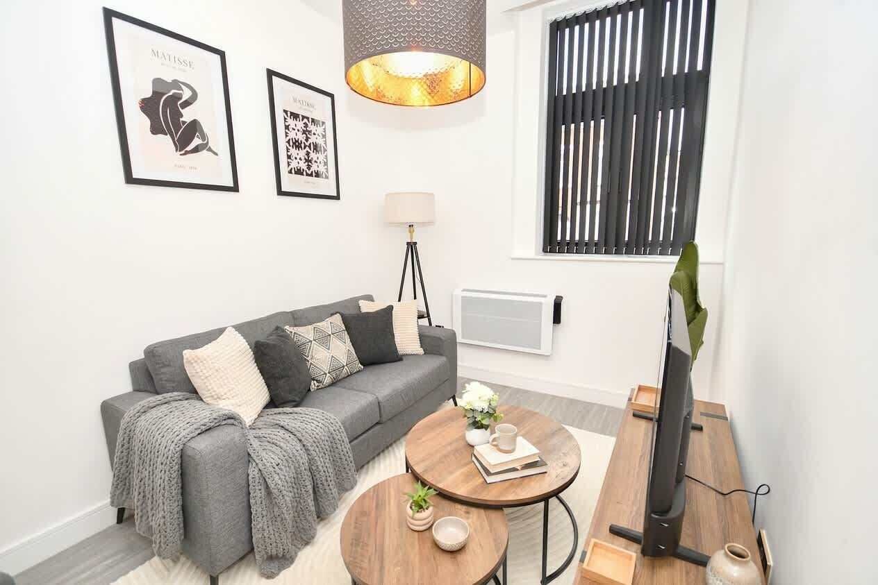 A modern living room with a grey sofa, a round coffee table, a TV on a wooden stand, and framed artwork on the wall.