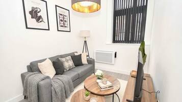 A modern living room with a grey sofa, a round coffee table, a TV on a wooden stand, and framed artwork on the wall.