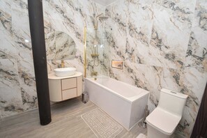 Une salle de bain avec un mur en marbre, une baignoire, des toilettes et un lavabo.