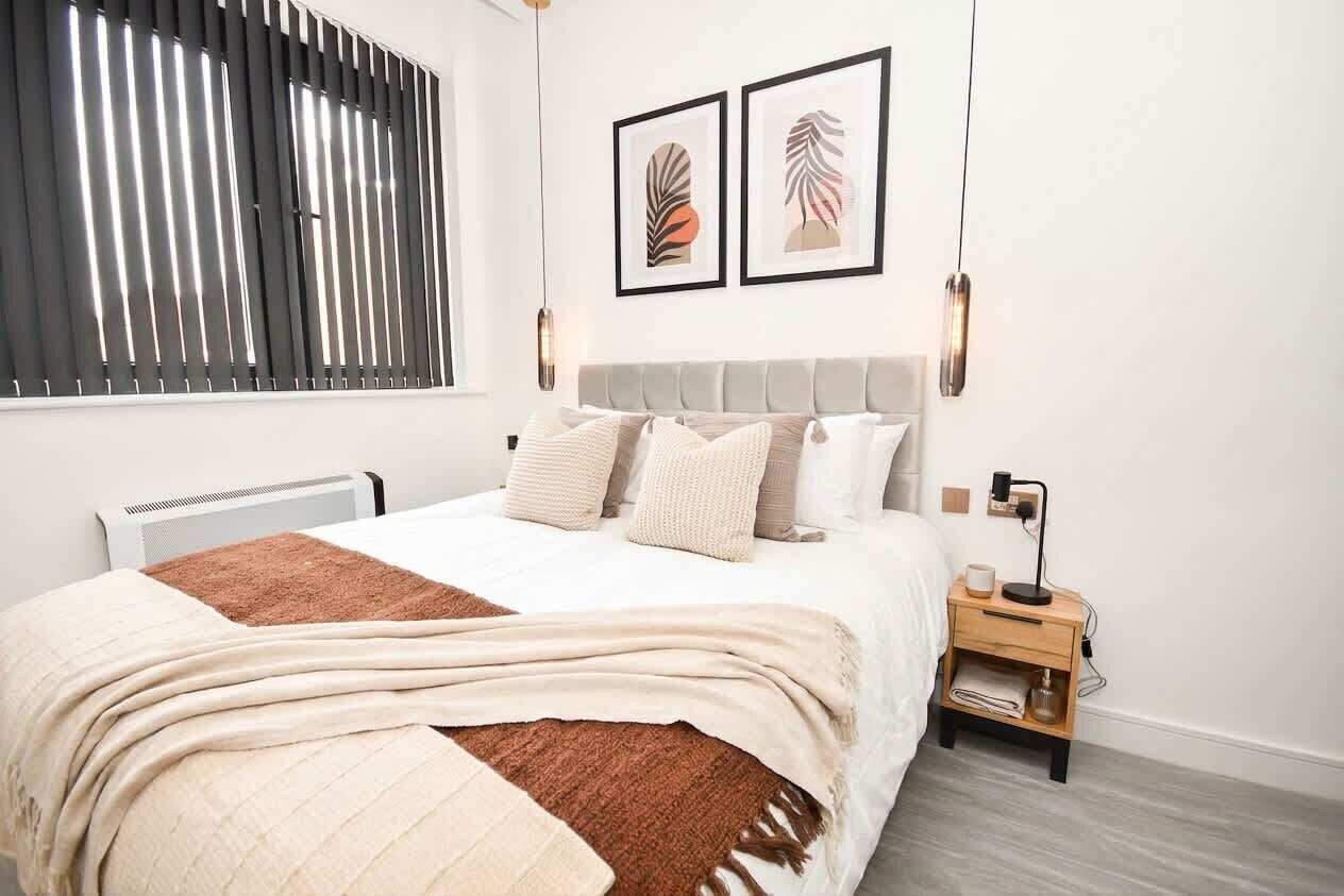 Ein Schlafzimmer mit einem Bett, einem Nachttisch, einer Wandlampe und zwei gerahmten Kunstwerken.