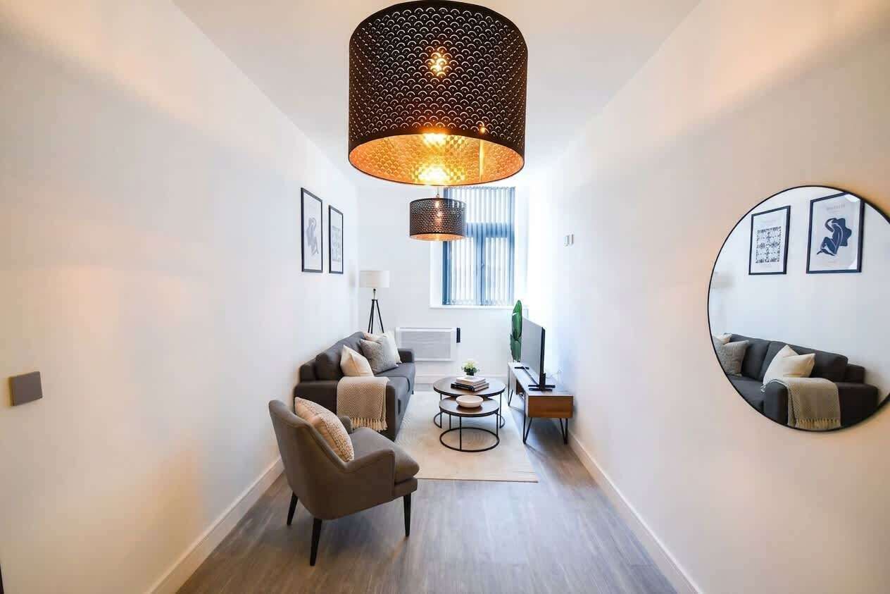 A modern living room with a sofa, armchair, coffee table, and a large circular mirror.