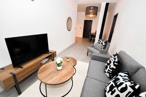A modern living room with a flat-screen TV, wooden coffee table, grey sofa, and patterned cushions. - Spacious 1 Bedroom Apartment in Central Wakefield (Wakefield)
