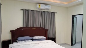 A bedroom with a bed, ceiling fan, air conditioning unit, and a view of the outside.